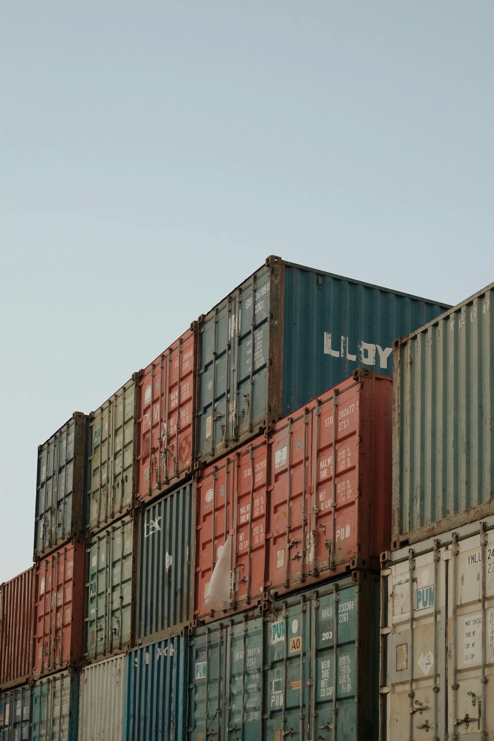 Stacked shipping containers in a port yard under a clear sky